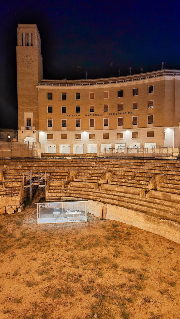 Ancient Roman Amphitheater in Lecce, Italy, at night with illuminated surrounding buildings.