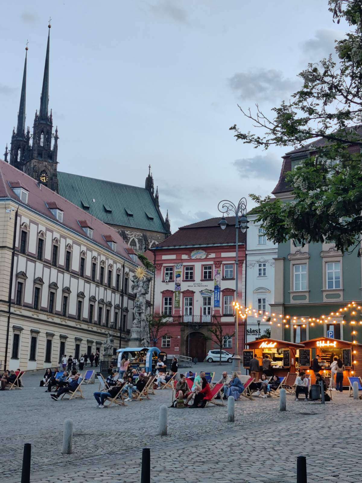 Evening atmosphere in Brno's main square with people relaxing in deck chairs under string lights.