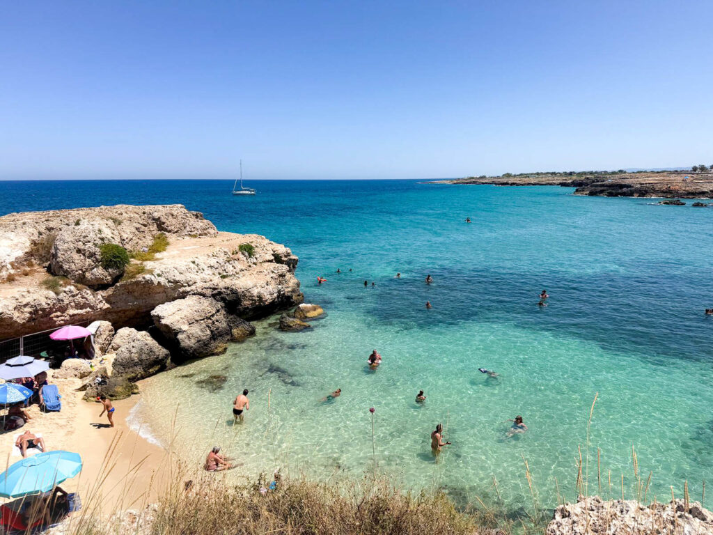Cala Paradiso beach in Monopoli, Puglia, with clear turquoise water and swimmers.
