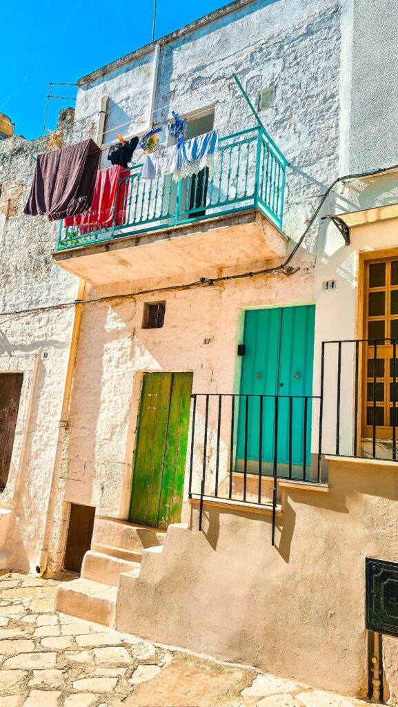 White-washed building with a turquoise balcony and colorful doors in Ceglie Messapica, Puglia.