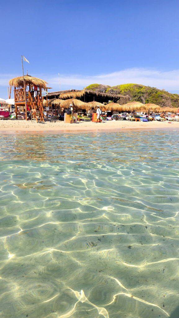 Crowded beach at Punta Prosciutto in Puglia with turquoise water and people swimming and sunbathing.