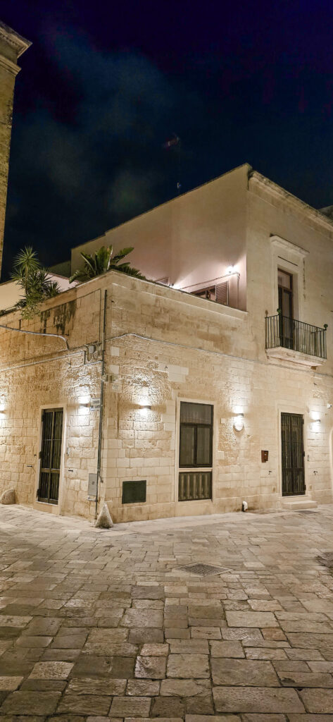 Illuminated stone buildings and a cobblestone street in Gallipoli, Puglia, at night.