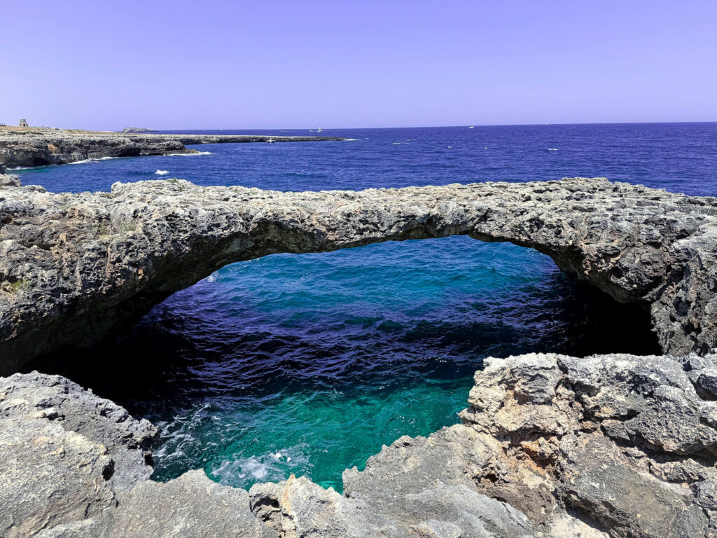 Natural rock archway over turquoise and deep blue sea at Grotticella Sella, Polignano a Mare.