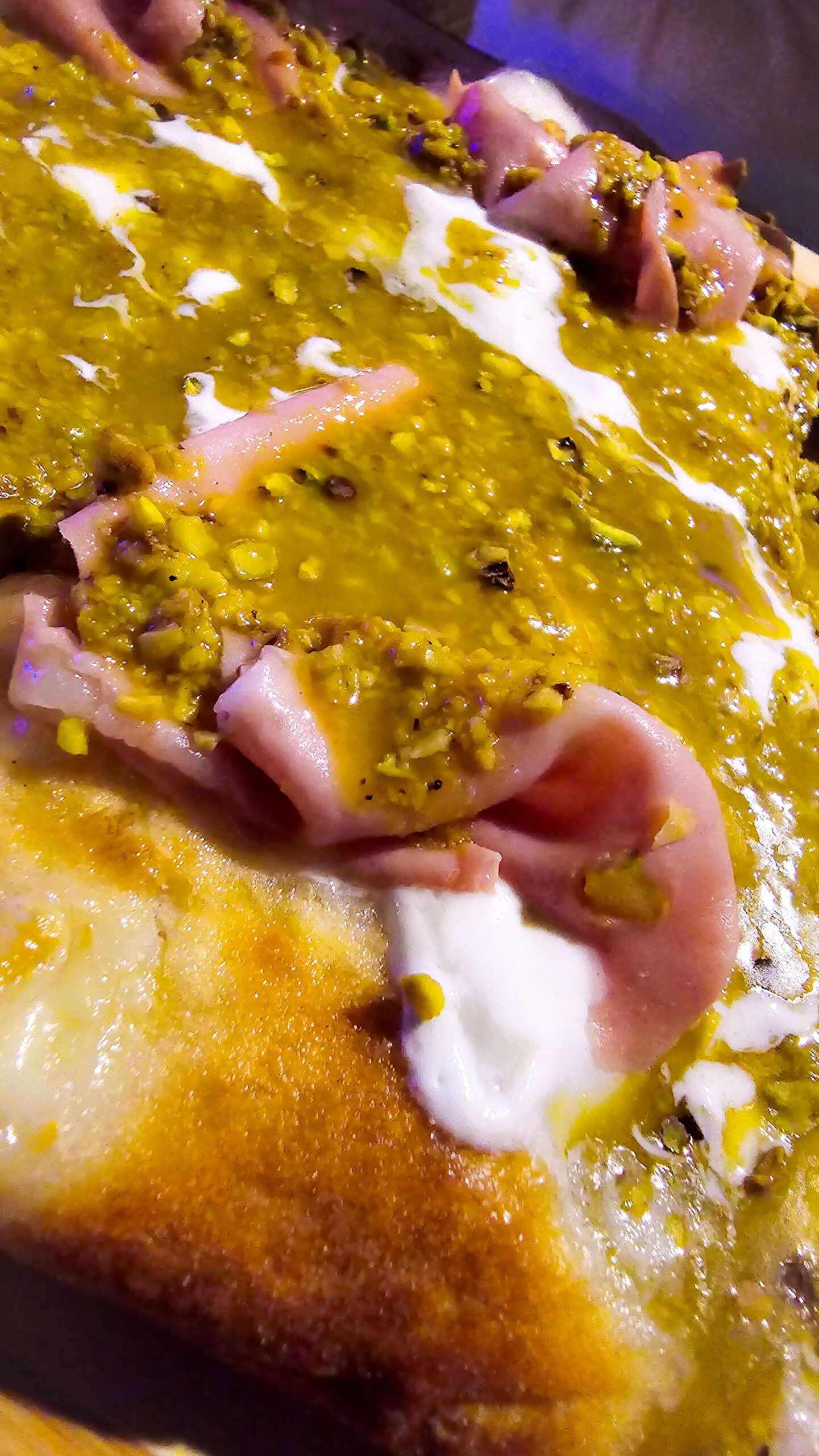 Close-up of a gourmet pizza topped with mortadella, pistachio cream, and burrata.