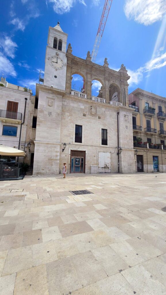 Palazzo del Sedile in Bari's old town, featuring a clock tower and archway, under a blue sky.

