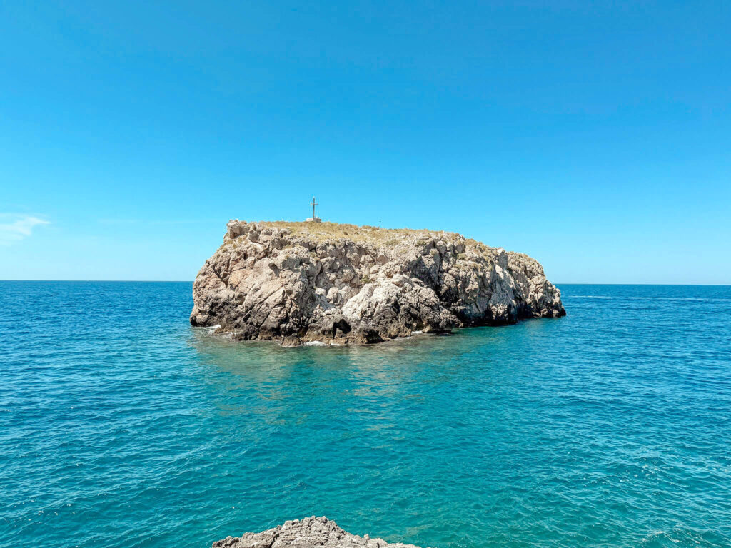 Scoglio dell'Eremita, a rocky islet with a cross, in the turquoise sea near Polignano a Mare.