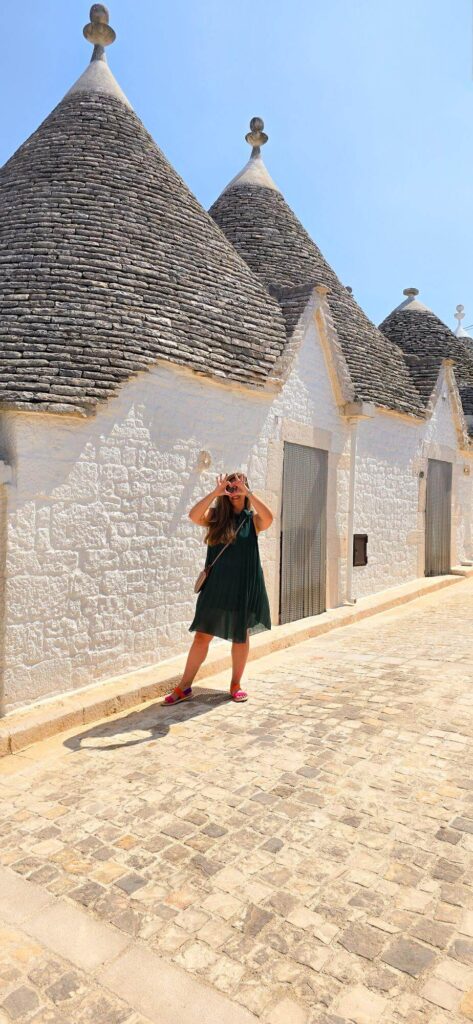 Woman posing in front of white trulli houses with conical roofs in Alberobello, Puglia.