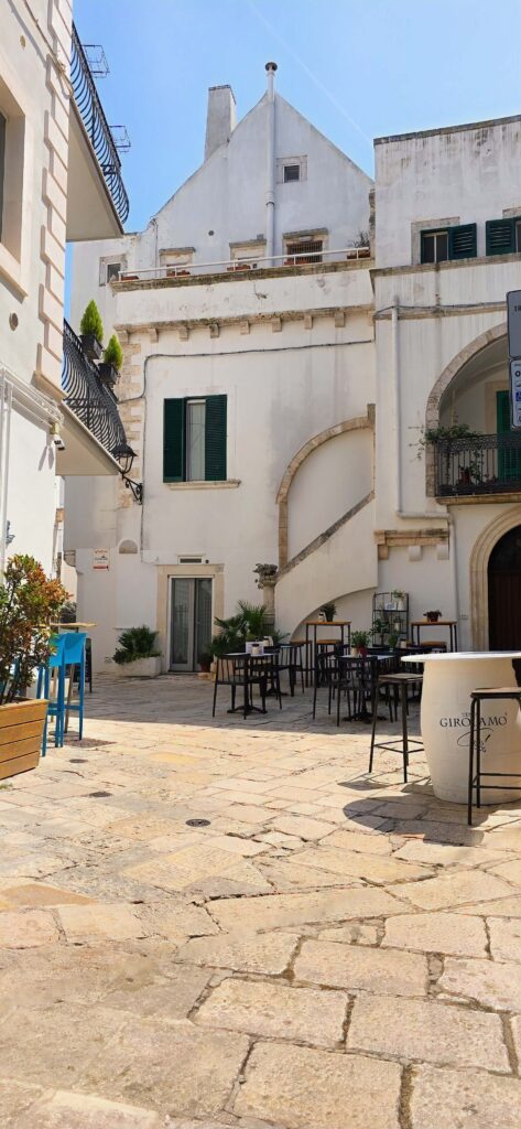 Quiet stone square in Locorotondo, Puglia, with white buildings and outdoor cafe seating. Example of what to do in Puglia