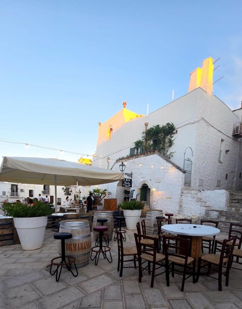 Outdoor seating at Brillo Parlante, a white-washed wine bar in Ceglie Messapica, Puglia, at dusk.