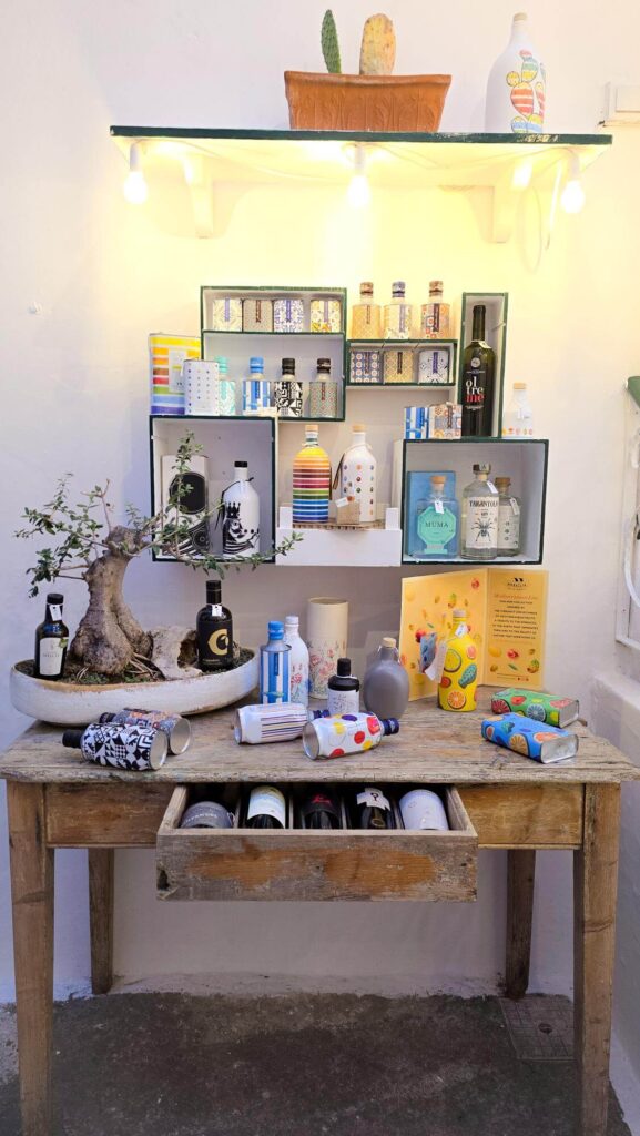 A rustic wooden table displaying a variety of colorful gin bottles and unique packaging at a gin shop in Ostuni, Puglia