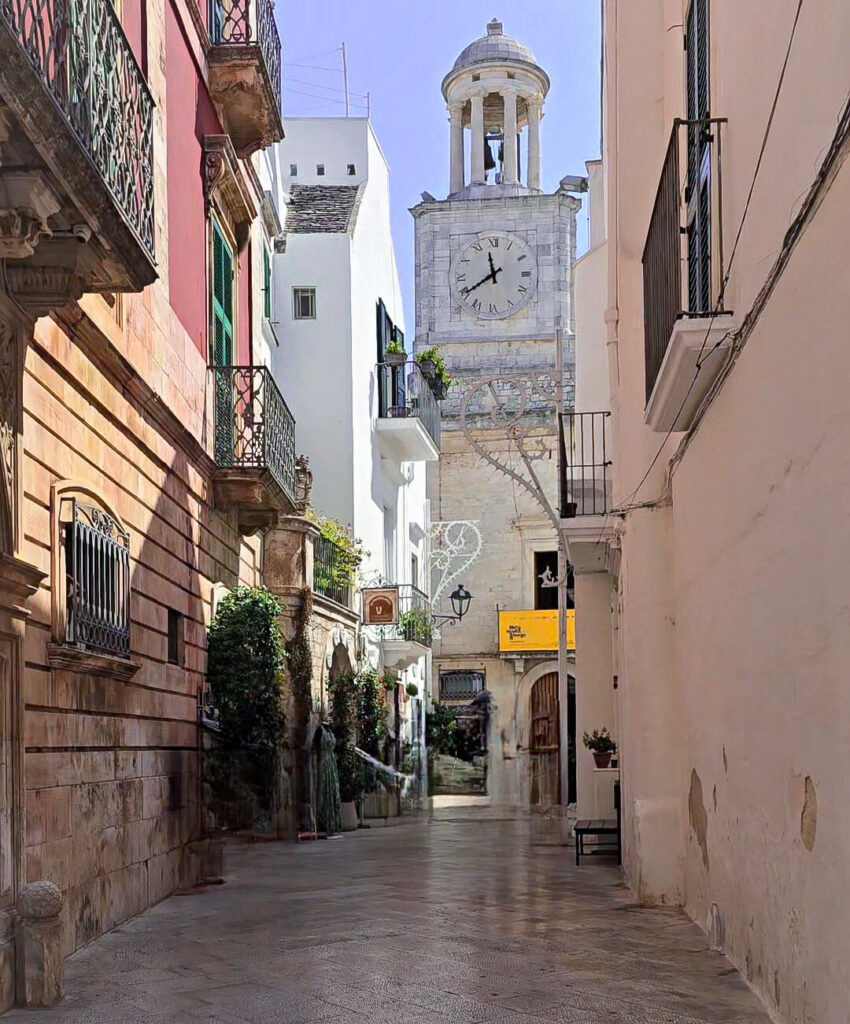 Narrow street in the center of Locorotondo, with a clock tower in the background.