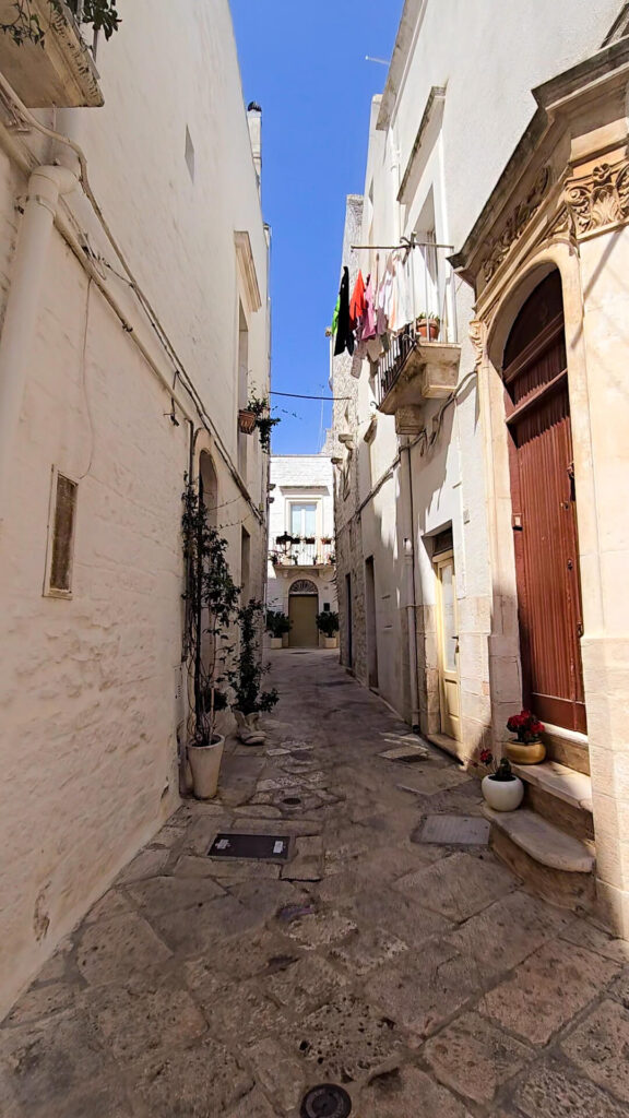 A narrow, clean street in Martina Franca with white buildings and laundry hanging from a balcony.