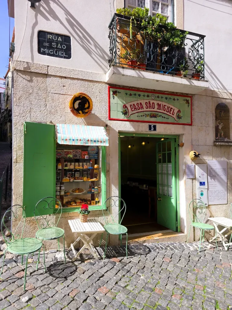 Charming café Casa São Miguel with green doors, outdoor chairs, and cobblestone streets in Alfama, perfect for brunch at Lisbon itinerary.