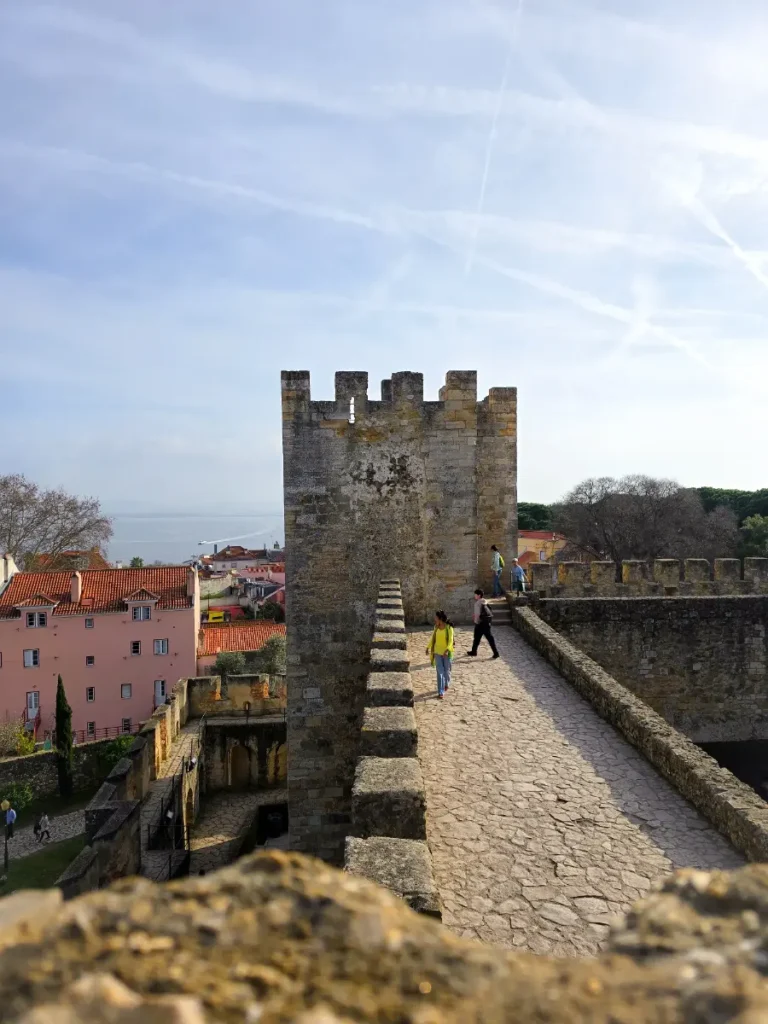 Stone walls and towers of Castelo de São Jorge in Lisbon with city and sea views in the background.