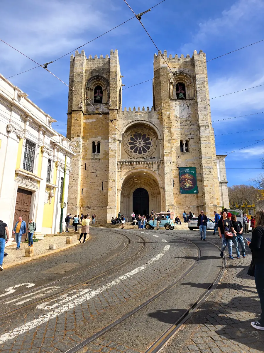 Front view of Lisbon Cathedral, also known as Sé de Lisboa, with tram tracks and people walking nearby.
