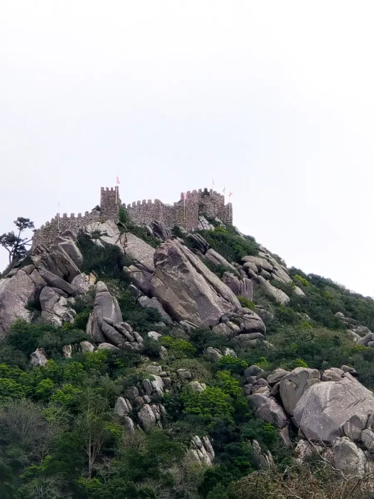 View of the Moorish Castle ruins on a rocky hilltop in Sintra, Portugal, surrounded by lush greenery.