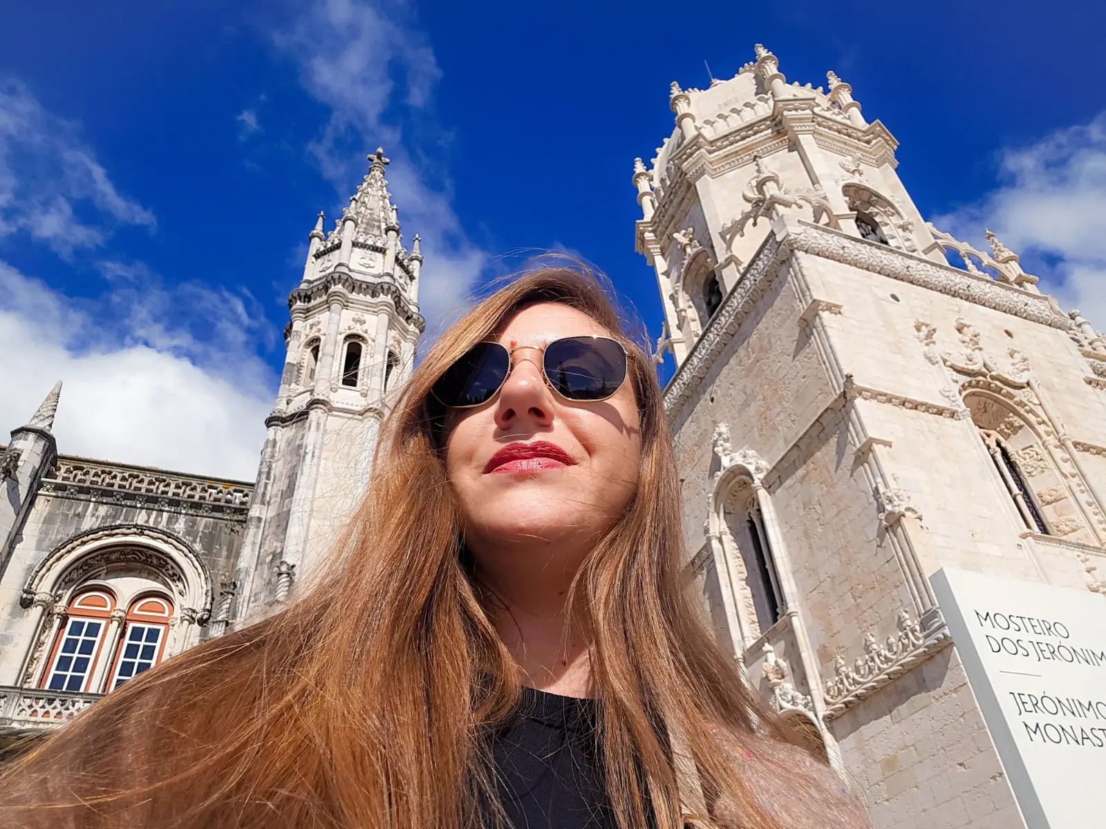 Traveler standing in front of Jerónimos Monastery in Belém, Lisbon, under a bright blue sky.