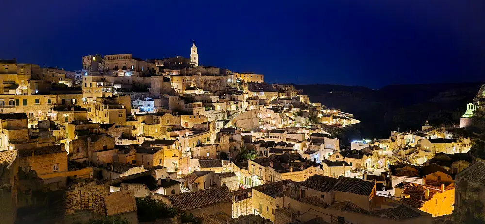 Matera’s Sassi illuminated at night with glowing stone houses and cathedral tower, part of Matera travel guide