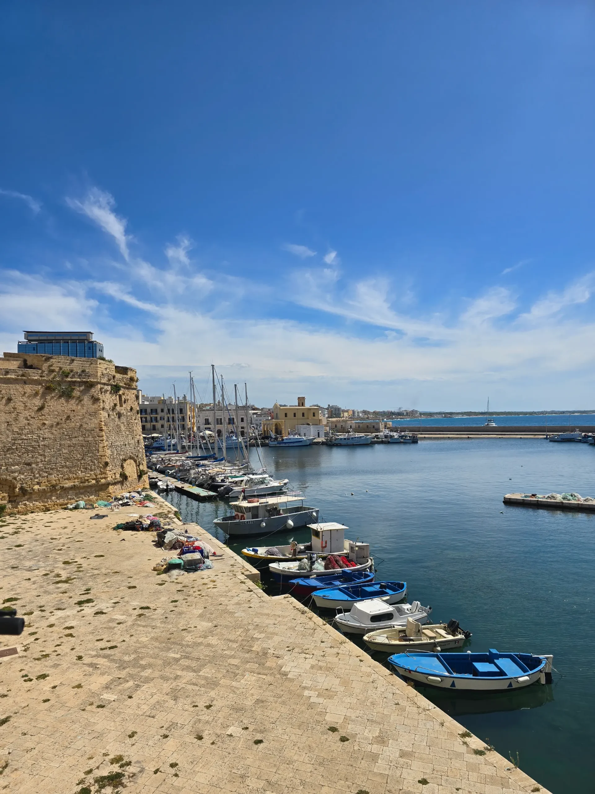 Traditional blue and white fishing boats moored in the turquoise waters of Gallipoli harbour next to the ancient stone city walls.