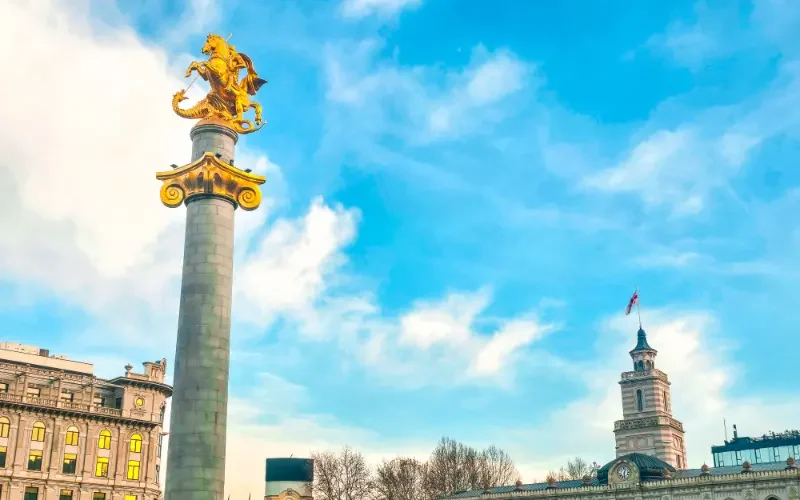 Tbilisi travel guide view of the golden St. George Liberty Monument and the historic City Assembly building in Freedom Square.