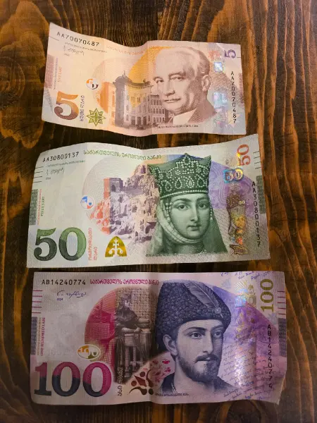 5, 50, and 100 Georgian Lari banknotes displayed on a wooden table.