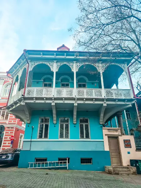 A bright blue historic house with ornate wooden balconies in Tbilisi.
