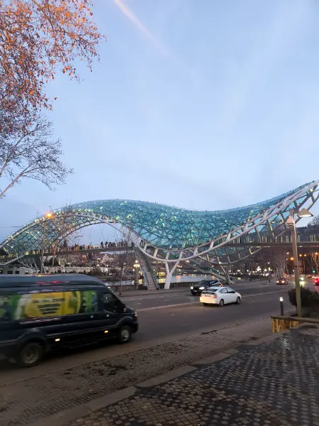 The glowing glass and steel Bridge of Peace over the Mtkvari River at dusk.